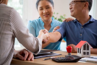 Happy couple elderly handshake with mortgage officer with agreement approve of buying home with loan, senior talking with agent real estate for planning while shaking hands, business and rent concept. clipart
