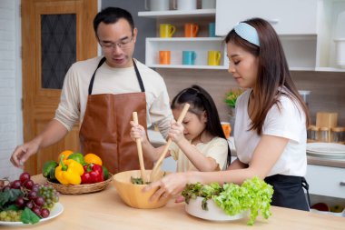Baba, anne ve kız birlikte mutlu Asyalı aile evde sebze salatası hazırlıyor, mutlu baba, anne ve çocuk salatayla kahvaltı hazırlıyorlar, yaşam tarzı konsepti.