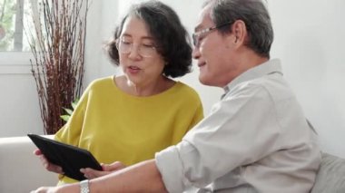 Mutlu son sınıf çifti koltukta oturup tablet kullanırken, video evde aile ile çevrimiçi arama yaparken, mutlu yaşlı erkek ve kadın aile ile uzak ve keyifli bir şekilde sohbet ediyorlar..