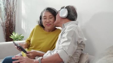 Mutlu aile çifti kulaklık takıyor müzik dinliyor ve evdeki sosyal medyada tablet izliyor, yaşlı erkek ve kadın rahatlıyor ve keyif alıyorlar, yaşam tarzları kavramlarıyla içli dışlı oluyorlar..