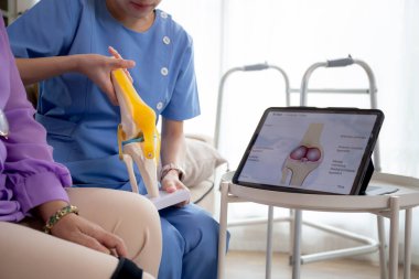 Evde tablet oturma odası, bakıcı ya da fizyoterapist olan yaşlı kadını açıklarken, tendon ve dizdeki artrit ve bacağındaki teşhis ve rehabilitasyonu kontrol etmeye yardım eden bakıcı ya da hemşire.