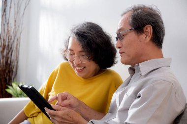 Mutlu son sınıf çifti koltukta oturup tablet kullanırken, video evde aile ile çevrimiçi arama yaparken, mutlu yaşlı erkek ve kadın aile ile uzak ve keyifli bir şekilde sohbet ediyorlar..