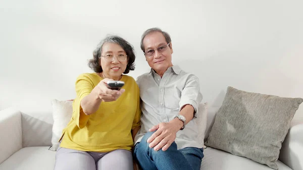 Happiness asian senior couple sitting on sofa watching TV with relax and enjoy in living room at home, happy family with elderly man and woman watching television, entertainment in weekend.