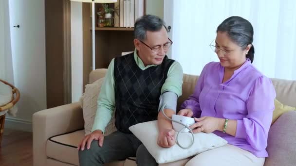 亚洲老年夫妇坐在沙发上检查血压 家里客厅里有压力表 老年男女坐在沙发上检查身体和压力 病人的医疗情况 — 图库视频影像