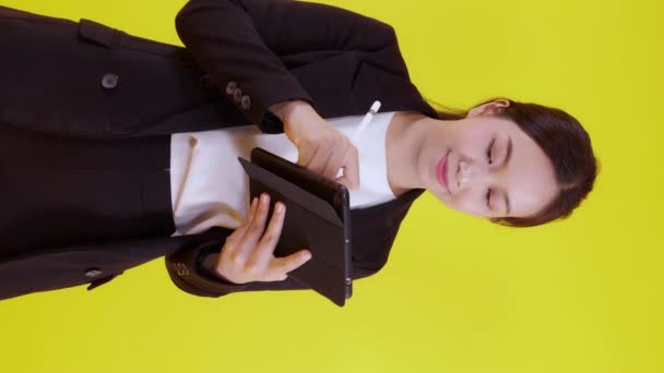 黄色の背景にインターネットに記録を書き込みタブレットを使用してスーツ姿の若いアジアの実業家の肖像 成功したデジタルタブレットを探しているビジネス女性 通信の概念 — ストック動画