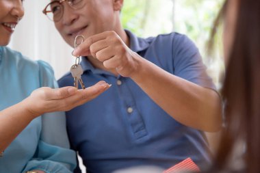 Emlakçı kadın, evde yaşlı bir çiftle, emlakçıyla ya da danışmanla birlikte ev anahtarlarını paylaşıyor. Mülkiyet ve sigorta konsepti için aile mirasının anahtarını veriyor..