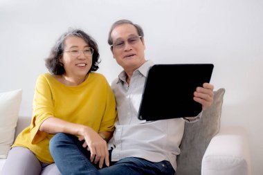 Mutlu son sınıf çifti koltukta oturup tablet kullanırken, video evde aile ile çevrimiçi arama yaparken, mutlu yaşlı erkek ve kadın aile ile uzak ve keyifli bir şekilde sohbet ediyorlar..