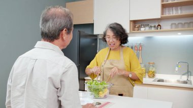 Asyalı son sınıf çifti evde, mutfakta sebze salatası yaparken, yaşlı bir aile yemek için salata hazırlarken tatmin olmuş, kaynaşmış ve ilişki kurmuş bir aile, yaşam tarzı konsepti..