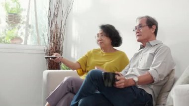 Mutlu Asyalı yaşlı çift kanepede oturup rahatça televizyon izliyor ve evde oturma odasında eğleniyor. Yaşlı bir adam ve kadınla birlikte mutlu bir aile hafta sonu televizyon seyrediyor..
