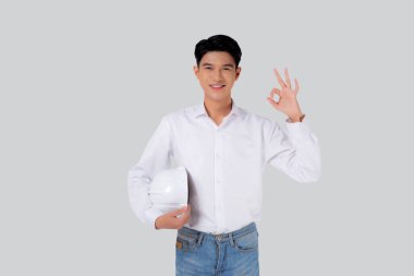 Miğfer tutan genç Asyalı mühendis gülümseyen ve hareket eden yakışıklı erkek mimar ya da müteahhit ya da işçi, endüstriyel konsept..