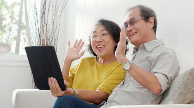 Mutlu son sınıf çifti koltukta oturup tablet kullanırken, video evde aile ile çevrimiçi arama yaparken, mutlu yaşlı erkek ve kadın aile ile uzak ve keyifli bir şekilde sohbet ediyorlar..