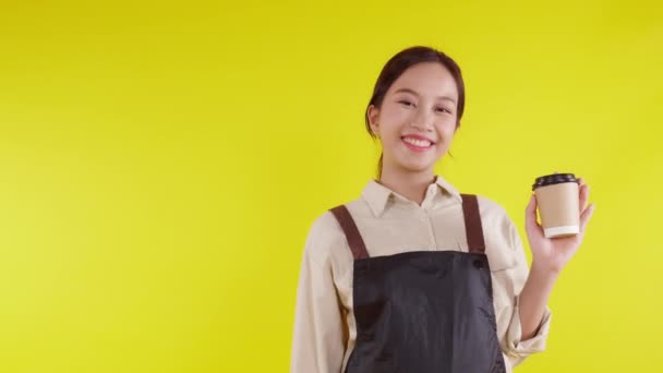 穿着围裙 拿着咖啡杯 背景是黄色的的的年轻的亚洲咖啡店女服务员 兴高采烈的女服务员 兴高采烈的小生意或初创企业 咖啡馆侍者 — 图库视频影像