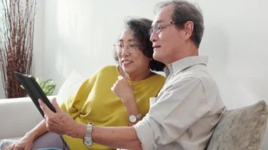 Mutlu son sınıf çifti koltukta oturup tablet kullanırken, video evde aile ile çevrimiçi arama yaparken, mutlu yaşlı erkek ve kadın aile ile uzak ve keyifli bir şekilde sohbet ediyorlar..