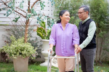 Asyalı son sınıf öğrencisi yaşlı kadına yardım ve destek olurken Walker 'la bahçede rehabilitasyon ve terapi için yürürken, yaşlı çift ve akrabalar, tıbbi konsept.