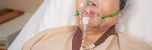 Patient elderly asleep with disease or unconscious in oxygen mask on bed at hospital ward, senior sick urgency in emergency room, respiration and lung, health and medicine, insurance and medical.