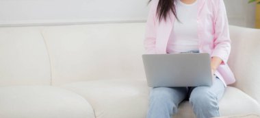 Genç Asyalı iş kadını evde dizüstü bilgisayarla çalışıyor oturma odasındaki kanepede internete bağlanıyor, serbest çalışan bir kadın dizüstü bilgisayar kullanıyor rahat ve rahat bir şekilde kanepede oturuyor, yaşam tarzı kavramı kullanıyor..