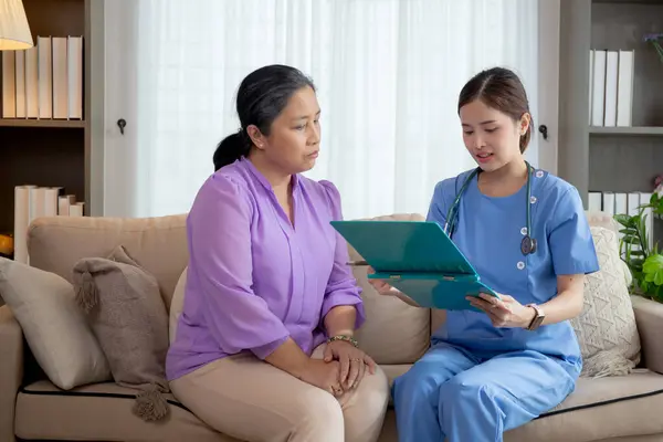 Caregiver sitting on sofa checkup and diagnostic with elderly woman patient about health in living room at home, caretaker sitting on couch explaining and examining senior, insurance and medical.