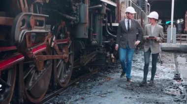 Takım elbiseli genç beyaz mühendis ve kadın tren istasyonunda tabletle kontrol ediyor. Mühendis sistem ulaşımını denetliyor. Teknisyen altyapıyı, ulaşımı ve endüstriyi inceliyor..