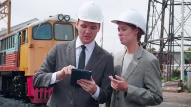 Takım elbiseli genç beyaz mühendis ve kadın tren istasyonunda tabletle kontrol ediyor. Mühendis sistem ulaşımını denetliyor. Teknisyen altyapıyı, ulaşımı ve endüstriyi inceliyor..