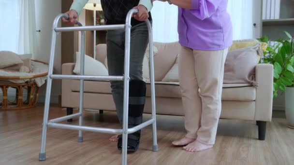小腿老年妇女帮助和支持老年男子 与散步者一起在家中客厅里散步进行康复和治疗 老年夫妇和亲戚 医疗观念 — 图库视频影像