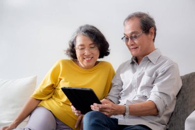 Mutlu son sınıf çifti koltukta oturup tablet kullanırken, video evde aile ile çevrimiçi arama yaparken, mutlu yaşlı erkek ve kadın aile ile uzak ve keyifli bir şekilde sohbet ediyorlar..