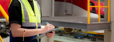 İstasyon, ulaşım ve altyapı panolarına bakım ve yazma belgesi için elektrik trenini kontrol eden genç mühendis veya işçi, müfettiş servis ulaşımını kontrol edin..
