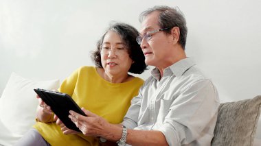 Mutlu son sınıf çifti koltukta oturup tablet kullanırken, video evde aile ile çevrimiçi arama yaparken, mutlu yaşlı erkek ve kadın aile ile uzak ve keyifli bir şekilde sohbet ediyorlar..