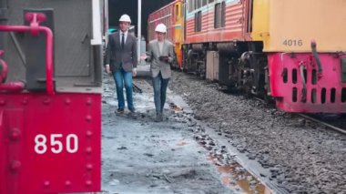 Takım elbiseli genç beyaz mühendis ve kadın tren istasyonunda tabletle kontrol ediyor. Mühendis sistem ulaşımını denetliyor. Teknisyen altyapıyı, ulaşımı ve endüstriyi inceliyor..