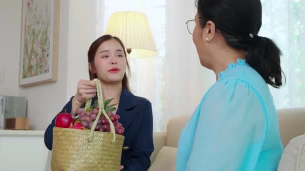 Fiatal Ázsiai Ügynök Biztosítás Látogatás Ügyfél Idős Miközben Gyümölcskosarat Nappaliban — Stock videók