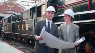 Takım elbiseli genç beyaz mühendis ve kadın tren şemasını kontrol ediyor. Ekip mühendisi sistem ulaşımını denetliyor. Altyapı, ulaşım ve endüstri teknisyeni..