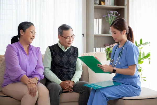 Caregiver sitting on sofa checkup and diagnostic with elderly couple patient about health in living room at home, caretaker sitting on couch explaining and examining senior, insurance and medical.