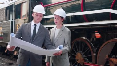 Takım elbiseli genç beyaz mühendis ve kadın tren şemasını kontrol ediyor. Ekip mühendisi sistem ulaşımını denetliyor. Altyapı, ulaşım ve endüstri teknisyeni..