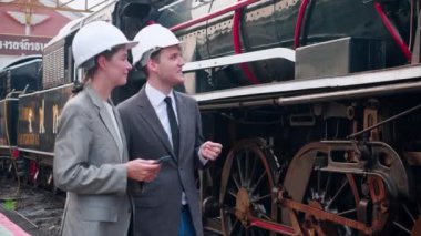 Takım elbiseli genç beyaz mühendis ve kadın tren istasyonunda tabletle kontrol ediyor. Mühendis sistem ulaşımını denetliyor. Teknisyen altyapıyı, ulaşımı ve endüstriyi inceliyor..