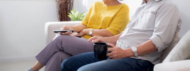 Mutlu Asyalı yaşlı çift kanepede oturup rahatça televizyon izliyor ve evde oturma odasında eğleniyor. Yaşlı bir adam ve kadınla birlikte mutlu bir aile hafta sonu televizyon seyrediyor..