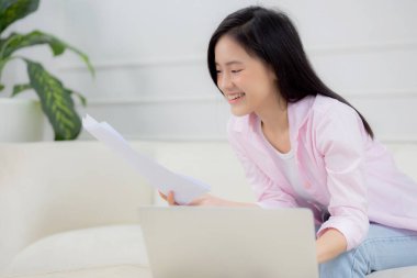 Young asian business woman working on laptop computer and looking graph and chart of report for profit on paper at home, businesswoman looking investment and income, data of infographic statistics.