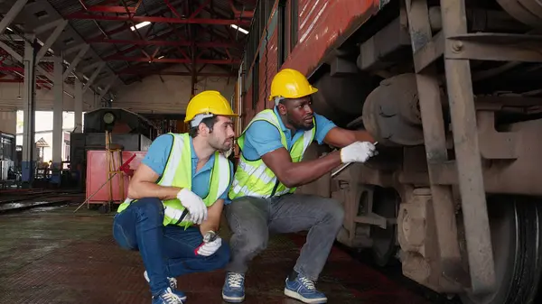 Young caucasian and black engineer maintenance and repair train diesel engine in station, team engineer inspect system transport, technician checking infrastructure, transportation and industry.