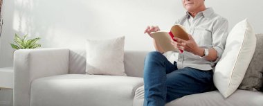 Asyalı son sınıf öğrencisi kanepede oturmuş kitap okuyor. Oturma odasında dinleniyor. Yaşlılar kanepede edebiyat okuyor..