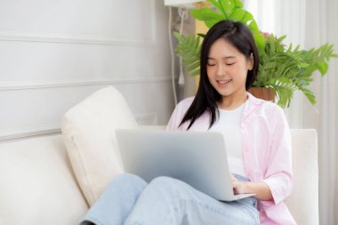 Genç Asyalı iş kadını evde dizüstü bilgisayarla çalışıyor oturma odasındaki kanepede internete bağlanıyor, defter kullanan serbest bir kız rahat ve rahat bir şekilde kanepede oturuyor, yaşam tarzı kavramı..