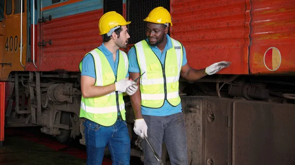Caucasian and black young engineer maintenance and repair train diesel engine in station, team engineer inspect system transport, technician checking infrastructure, transportation and industry.