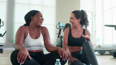 Spor salonunda konuşan iki genç kadın, spor giyim ve arkadaş veya koç rahatlayıp spor yaparken sağlık, çeşitlilik ve etnik köken, spor konsepti için egzersiz ve egzersiz yaparken tartışıyorlar..