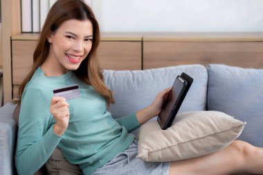 Genç Asyalı bir kadın dijital tablet alışverişini internet üzerinden yapıyor. İnternete kredi kartı satın alıyor. Kanepe, satın alma ve ödeme, iş ve yaşam tarzı ile kadın ödemesi yapıyor..