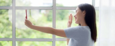 Genç Asyalı mutlu kadın videosu, akıllı telefonuyla evdeki oturma odasında, gülümseyen ve sosyal medyayı evdeki akıllı telefonuyla, yaşam tarzıyla ve iletişim konseptiyle kullanan kadın..