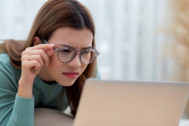 Yoğunlaşmış Asyalı gözlüklü genç bir kadın dizüstü bilgisayarla çalışıyor. Bağlılık ve hırsla çalışıyor. Oturma odasında koltukta oturuyor, evden çalışıyor, serbest çalışıyor..