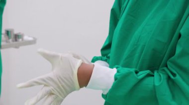 Doktor ya da cerrah eldiven giyip ameliyathanede acil ameliyat hazırlıyor. Takım çalışması yapan bir grup cerrah, çeşitlilik, etnik köken, tıp ve bilim kavramına sahip üniforma giyiyor..