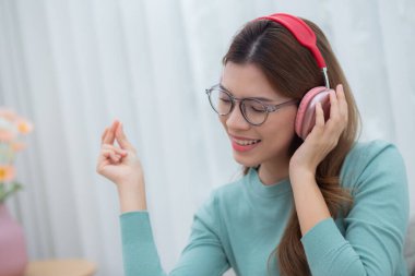 Kulaklık takmış, müzik dinleyen mutlu genç bir kadın. Oturma odasında eğleniyor ve eğleniyor. Eğlence dolu mutlu bir kadın, bir kişi, yaşam tarzı konsepti..