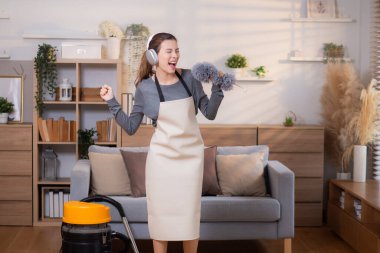 Genç Asyalı bir kadın, kulaklıkla müzik dinlerken, oturma odasında temizlik yaparken, ev işi yaparken, evde toz alırken, şarkı söylerken, ev işi yaparken, yaşam tarzı konsepti.