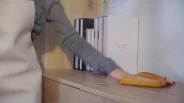 Yakın plan genç Asyalı kadın önlük giyip oturma odasındaki ahşap dolabın tozunu alıyor, yakın plan kadın temizlik yapıyor, yaşam tarzı konsepti..