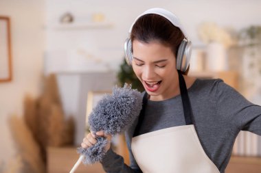 Genç Asyalı bir kadın, kulaklıkla müzik dinlerken, oturma odasında temizlik yaparken, ev işi yaparken, evde toz alırken, şarkı söylerken, ev işi yaparken, yaşam tarzı konsepti.