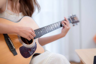 Genç Asyalı bir kadının evdeki kanepede oturup gitar çalması, yetenek ve pratik yapması, gitarist ve hobisi zevkli ve rahatlatıcı, eğlence ve yaşam tarzı..