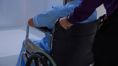 Genç Asyalı adam asansörle düğmeye basarken yaşlı baba hastanede tekerlekli sandalyede oturuyor, kıdemli baba ve oğlu tekerlekli sandalyeyle asansöre, sağlık ve sigortaya gidiyor..